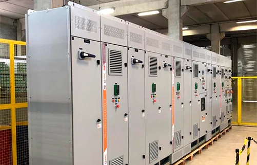 Painéis elétricos industriais da AMC Soluções em galpão de montagem, com fileiras simétricas de quadros de comando.