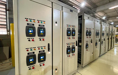 Painéis elétricos industriais da AMC Soluções em galpão de montagem, com fileiras simétricas de quadros de comando.