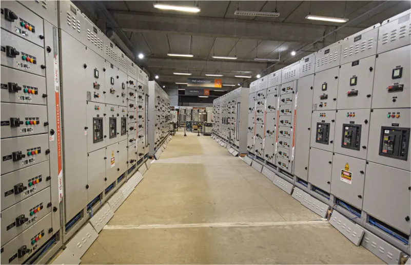 Painéis elétricos industriais da AMC Soluções em galpão de montagem, com fileiras simétricas de quadros de comando.